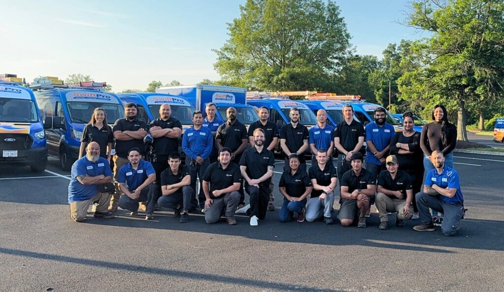 The SwiftPro heating, cooling and plumbing team lined up in front of a row of wrapped SwiftPro vans at the Chantilly, Virginia shop