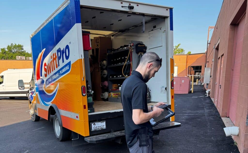A SwiftPro technician checking a work order on a tablet behind a stocked SwiftPro service truck at a commercial building in Northern Virginia