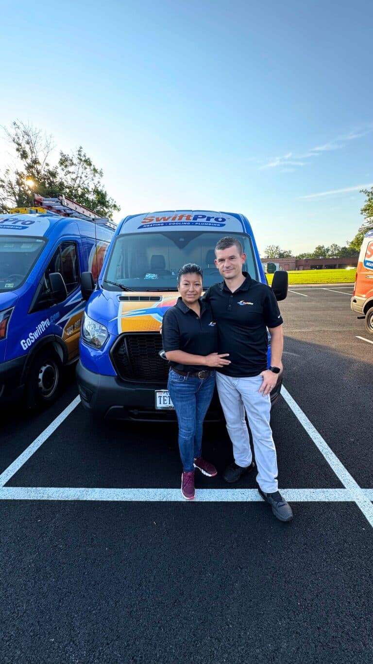 Two members of the SwiftPro team, a man and a woman in black company polos, standing in front of a wrapped SwiftPro service van in a Northern Virginia parking lot