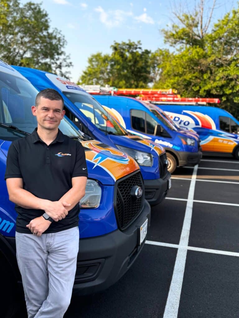 Tyler Griffin, owner of SwiftPro, in a black SwiftPro polo leaning on a wrapped SwiftPro van at the front of a row of company vans in Northern Virginia