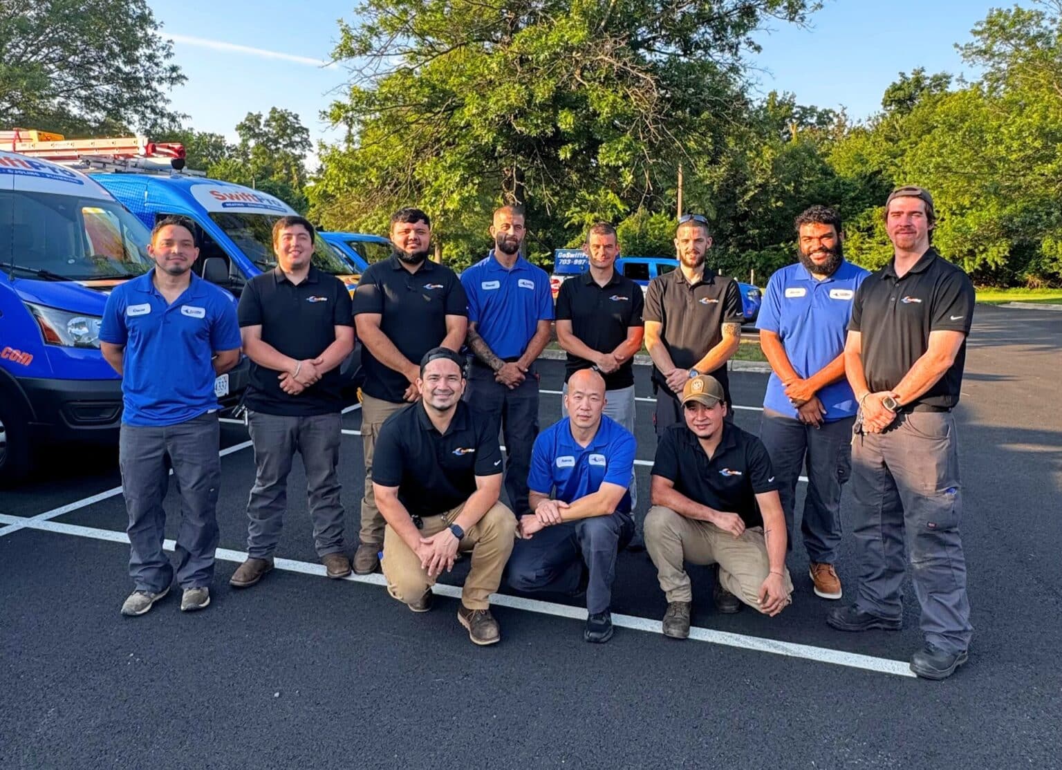 SwiftPro heating, cooling and plumbing technicians in SwiftPro polos, standing and kneeling in front of the company's wrapped vans in Northern Virginia