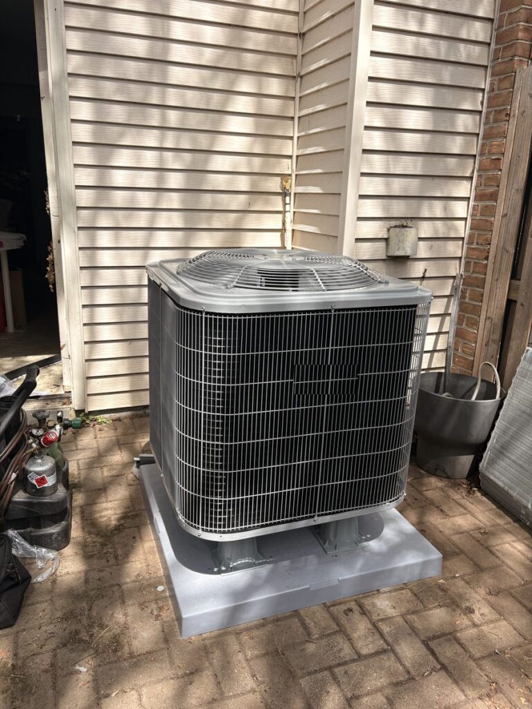A new outdoor air conditioner on a new grey pad over a brick patio beside a sided home in Alexandria, Virginia, set by SwiftPro on an AC replacement, refrigerant cylinders and tools beside it