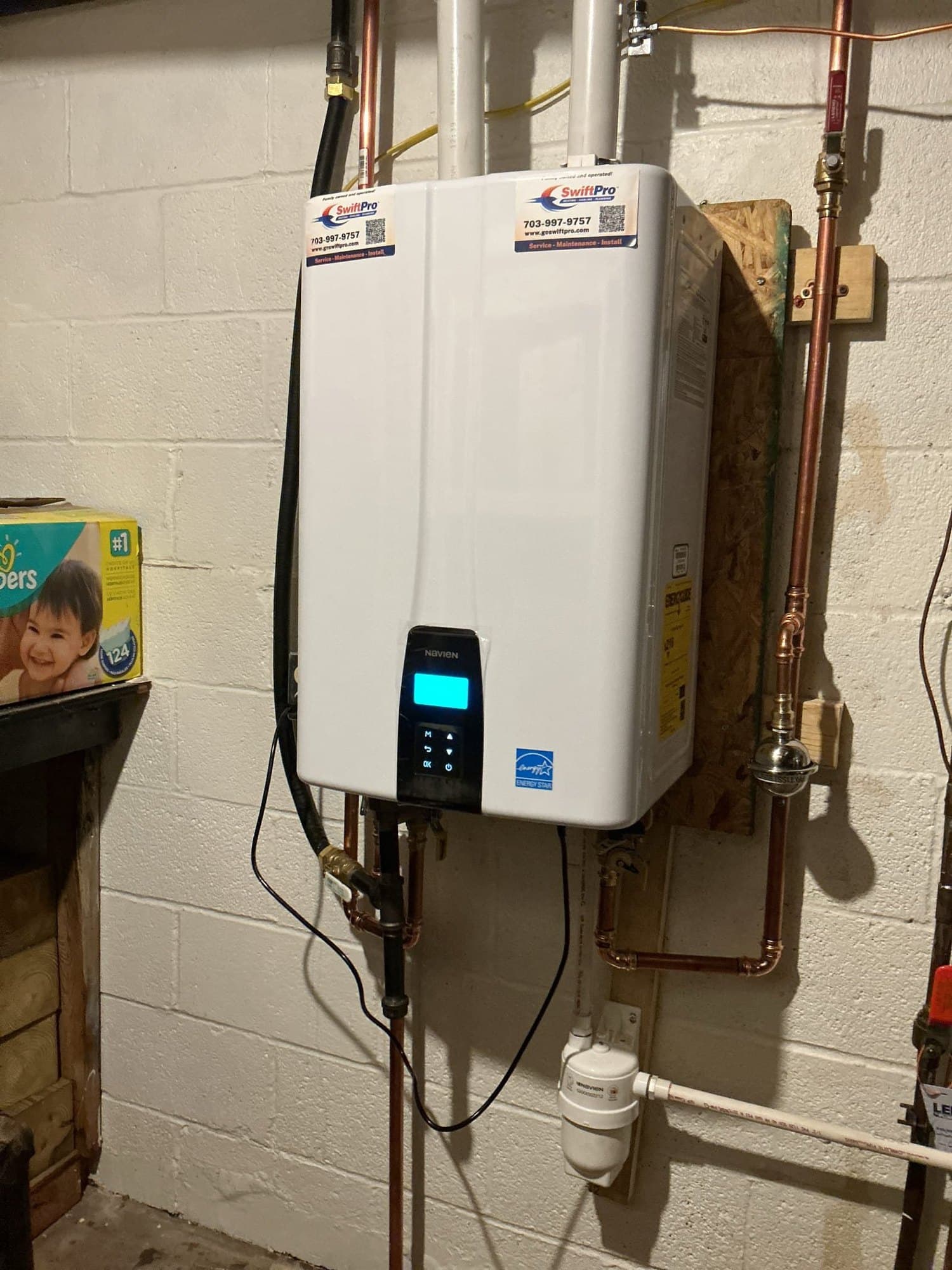 A wall-mounted Navien tankless water heater installed by SwiftPro in a Northern Virginia basement, with the condensate trap and gas line run to it