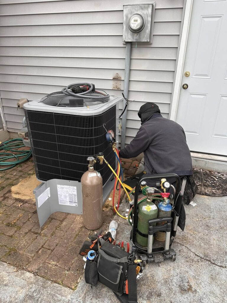A SwiftPro technician kneeling at an outdoor condenser with refrigerant recovery tanks and gauges