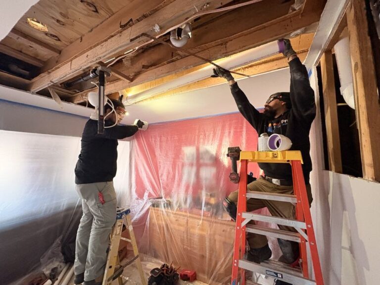 Two SwiftPro technicians working overhead on ceiling ductwork behind protective sheeting.