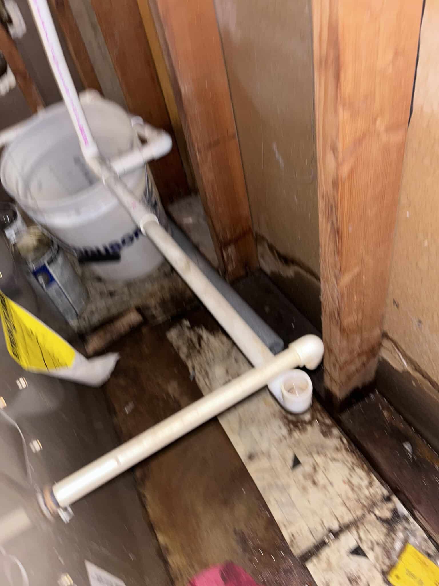 Exposed plumbing with white pipes and a bucket in a dimly lit area