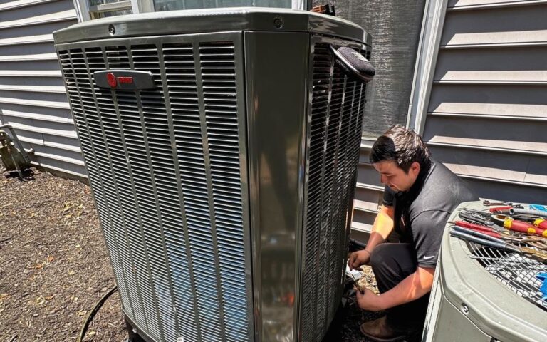 A SwiftPro technician kneeling beside a Trane outdoor air conditioning unit at a Northern Virginia home, working at the base of the cabinet, his tools laid out on the older unit beside it