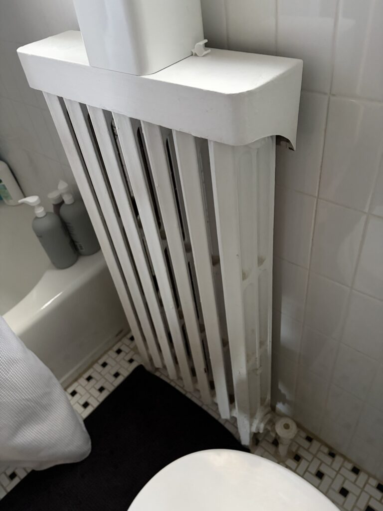 A painted cast iron radiator in a tiled bathroom of a Northern Virginia home, the heat emitter on a hot water boiler system