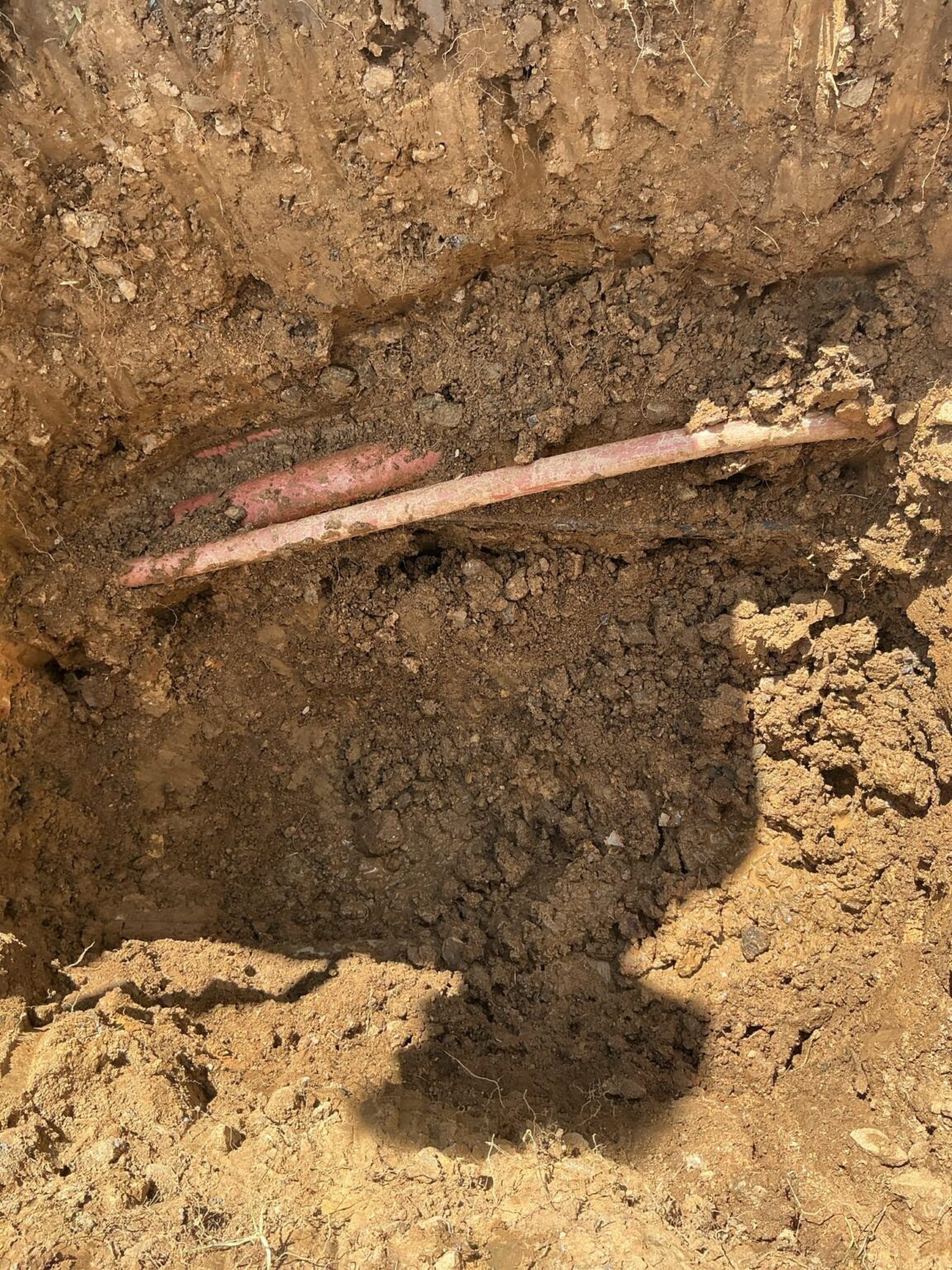 An excavated trench in a Northern Virginia yard exposing the buried copper water service line during a SwiftPro repair