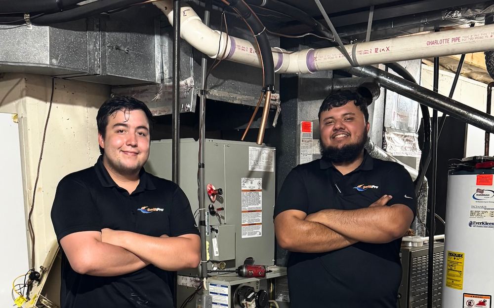 Two SwiftPro technicians in a basement mechanical room beside a furnace and a gas water heater