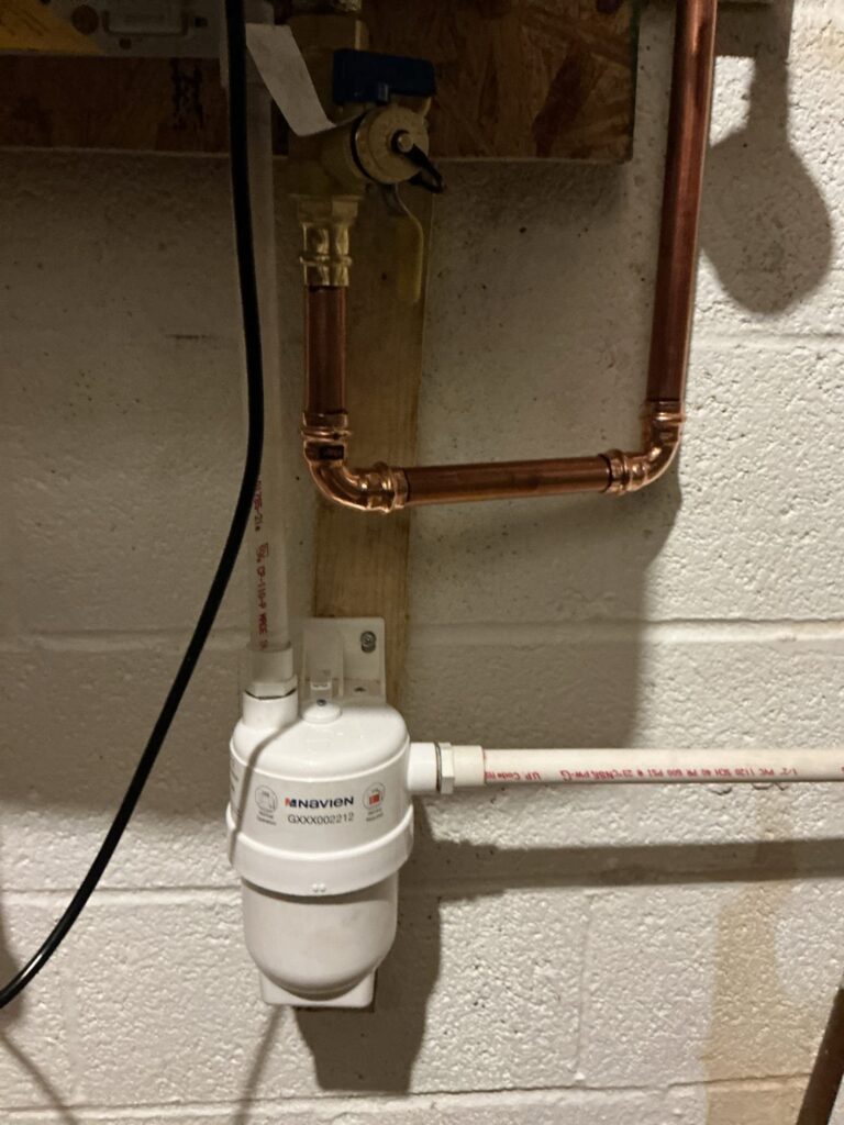 A Navien condensate neutralizer plumbed on a basement wall below a tankless water heater in Northern Virginia