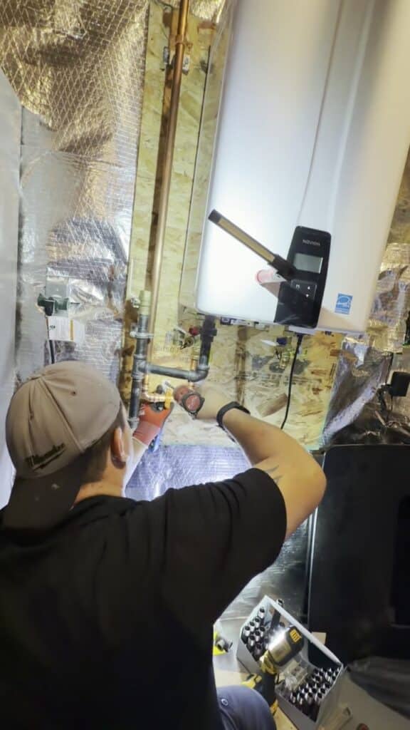 A SwiftPro plumber working on the water and gas connections under a Navien tankless water heater in a Northern Virginia basement