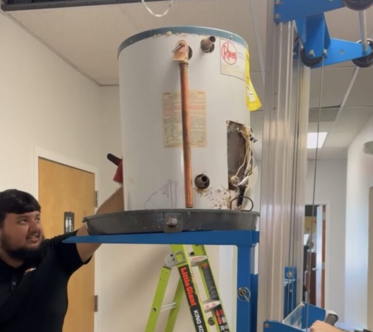 A SwiftPro plumber taking an old, rusted Rheem tank water heater down on a lift in Northern Virginia, the Rheem label on the front of the tank