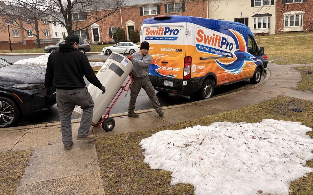 Two SwiftPro plumbers wheeling a tank water heater from a wrapped SwiftPro van to a townhouse in Northern Virginia