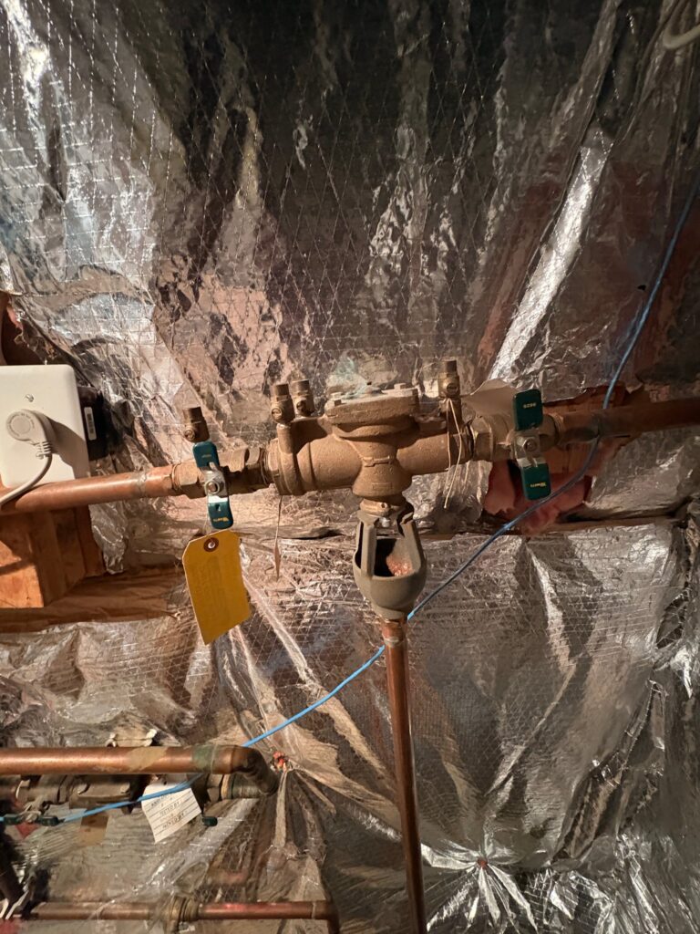 An old, corroded RPZ backflow preventer on copper pipe in a Loudoun County, Virginia basement, before SwiftPro replaced it