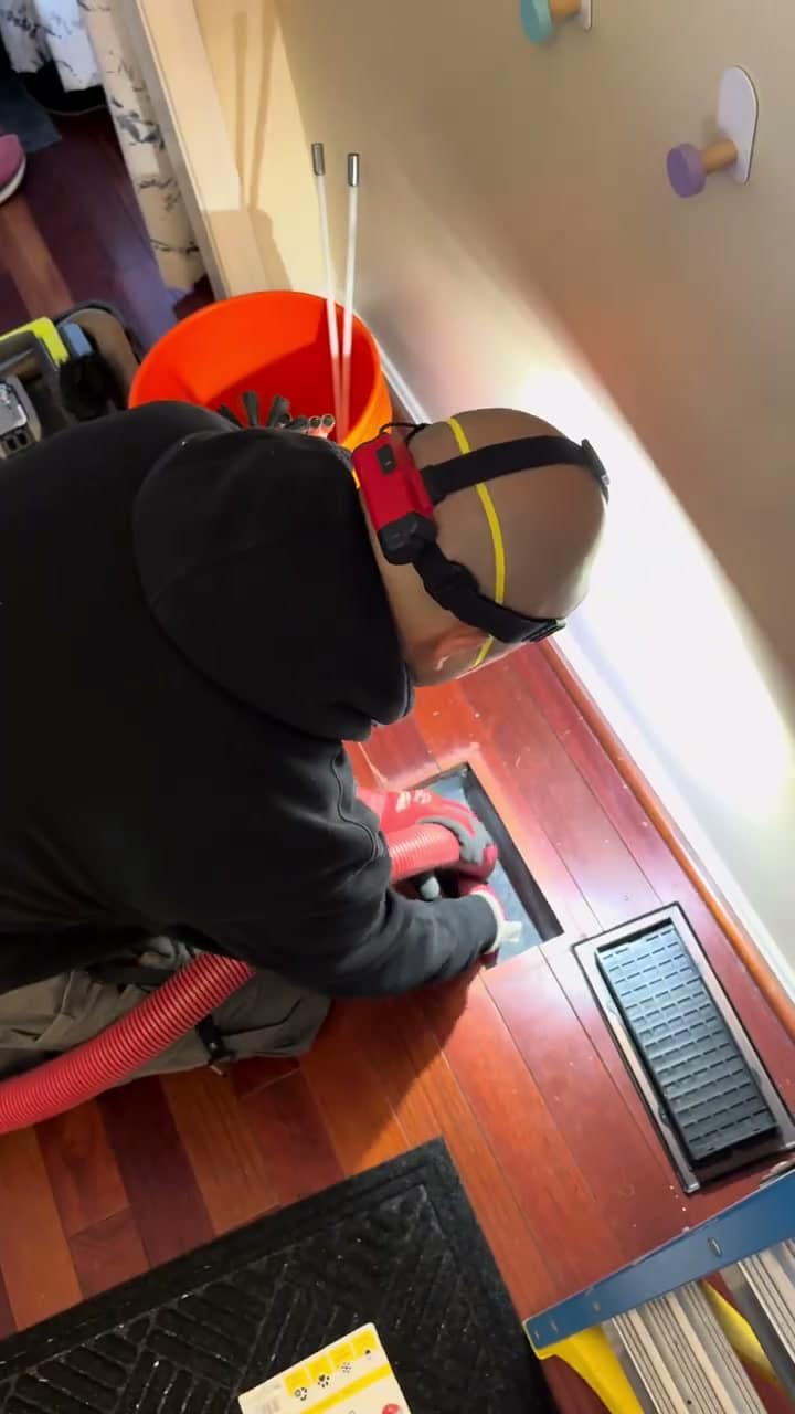 A SwiftPro technician kneeling at a floor register in a Northern Virginia home, running the vacuum hose into the duct below it