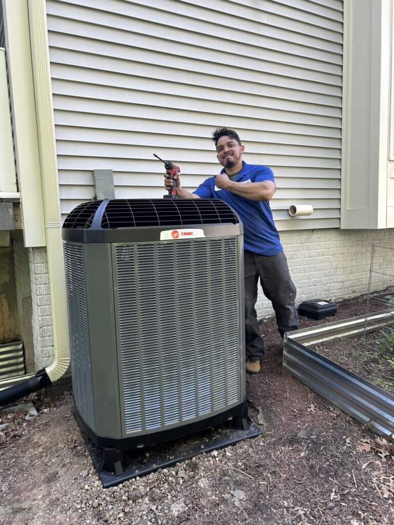 A SwiftPro technician in a blue company shirt beside a newly installed Trane outdoor unit on a level pad against a Northern Virginia house