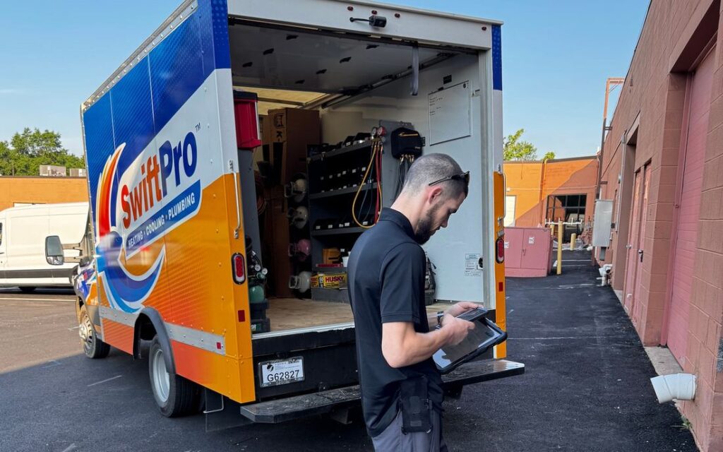 A SwiftPro technician reading a tablet at the back of an open SwiftPro box truck