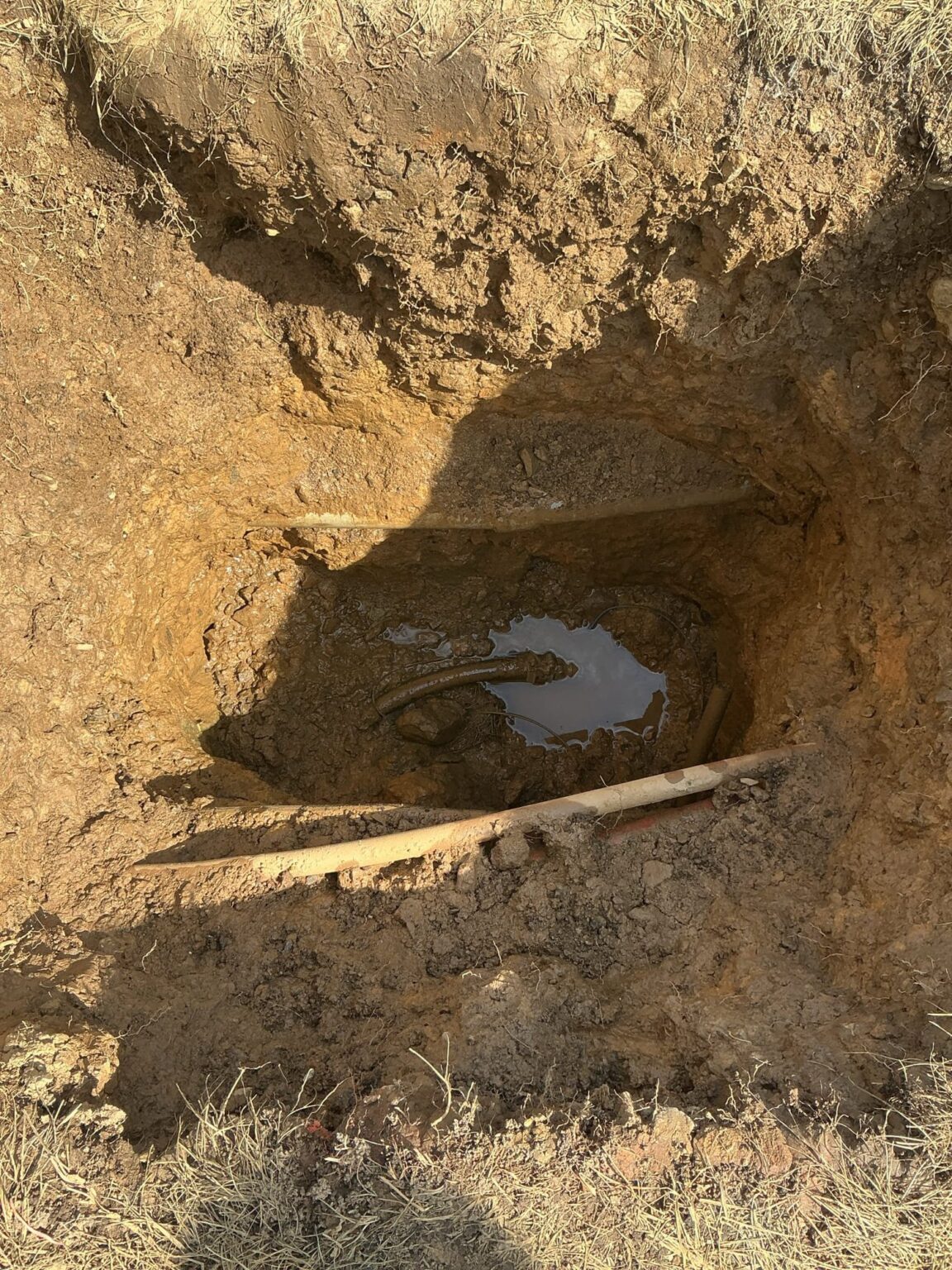 A dug trench in a Northern Virginia yard with water pooling around the failed underground sewer pipe SwiftPro is replacing