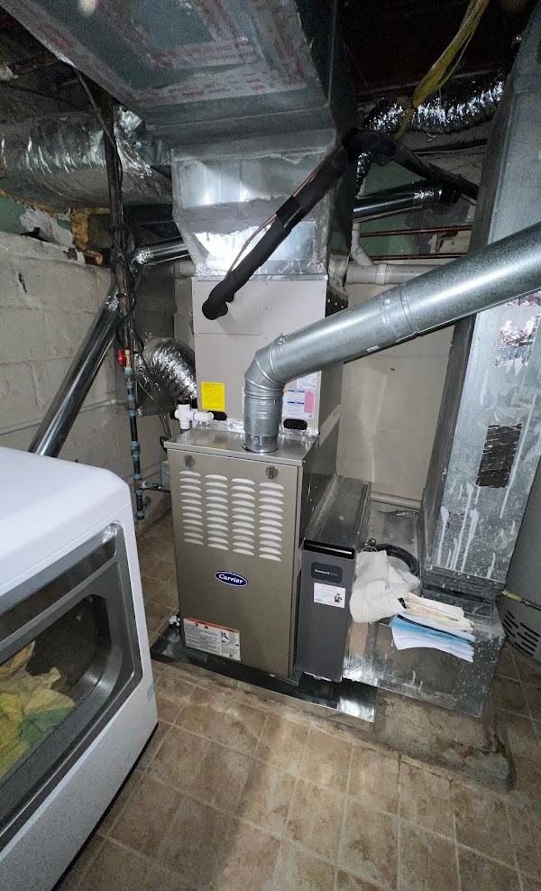 A Carrier gas furnace with its coil and flue above it in a Northern Virginia basement, a media air cleaner cabinet on its return side, on a SwiftPro job