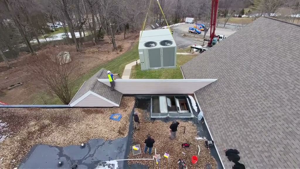 Drone and ground footage of a crane lifting an old Trane rooftop unit off a commercial building and setting a new one on the curb.