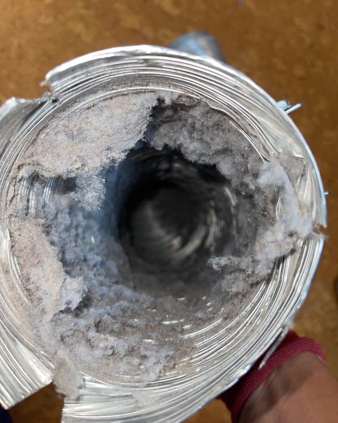 A foil dryer vent hose held up by a SwiftPro technician, its inside walls caked with grey lint, from a dryer vent cleaning in Northern Virginia
