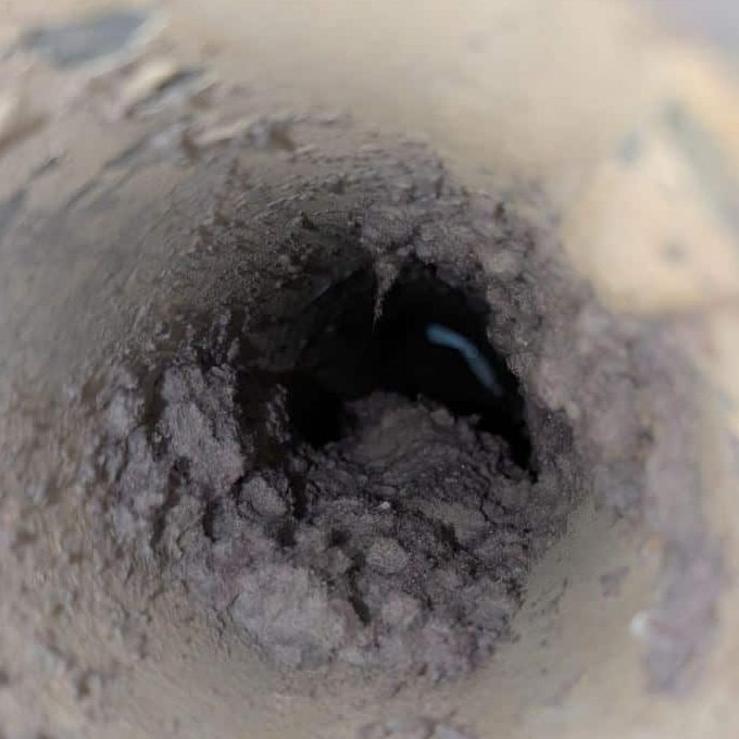 Looking down a dryer vent line in Ashburn, Virginia before a SwiftPro dryer vent cleaning: the opening is packed with grey lint