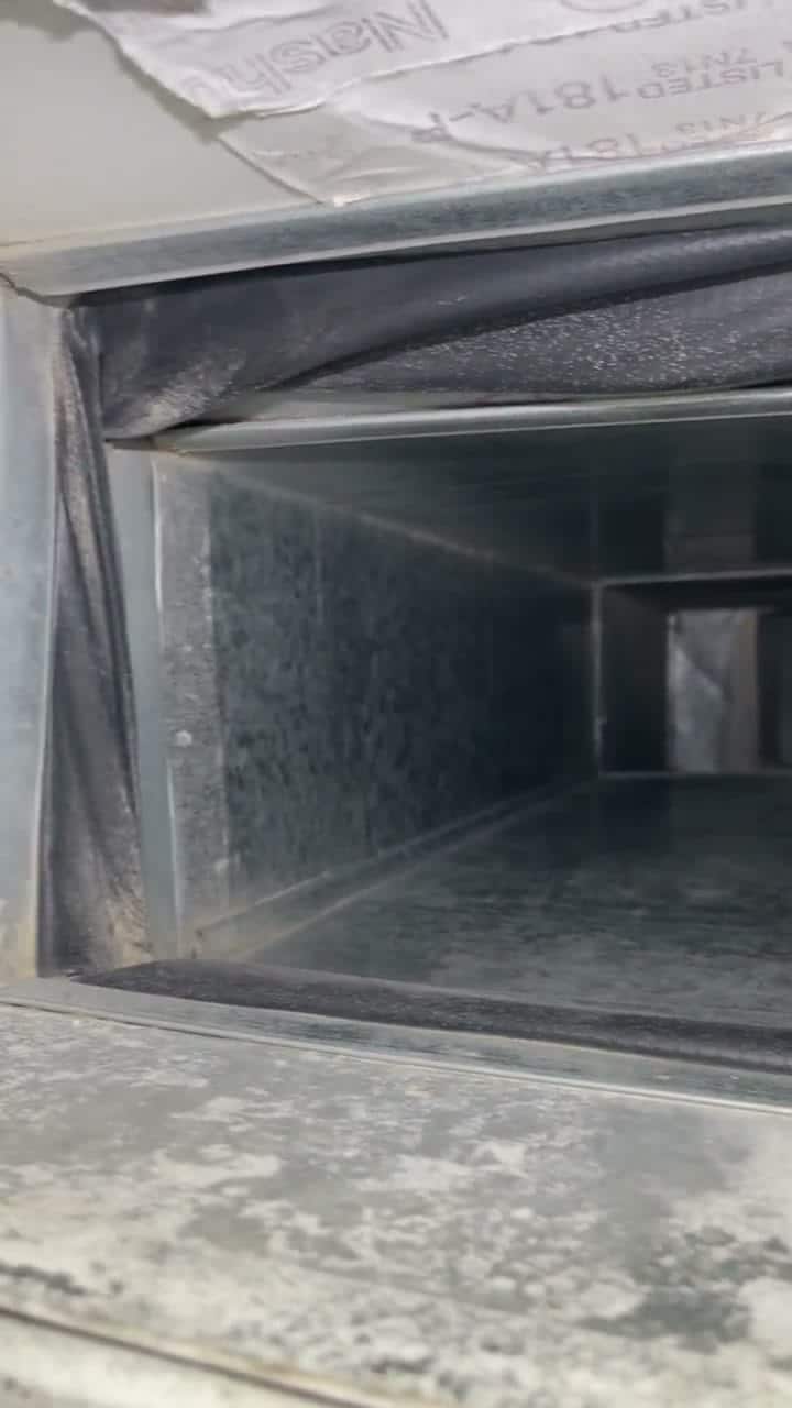 Raw phone clip, no text: looking down a supply trunk with dust patches on the floor and a loose flex connector at the end.