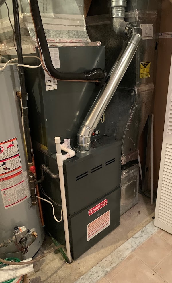 A Goodman gas furnace in a Northern Virginia utility closet with new flue piping, beside a gas water heater, on a SwiftPro job