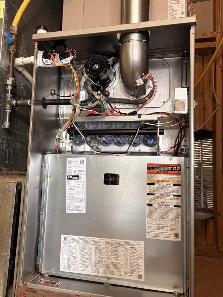 A new gas furnace with its front panel off in a basement in Ashburn, Virginia, its burners, inducer and metal vent pipe visible, installed by SwiftPro