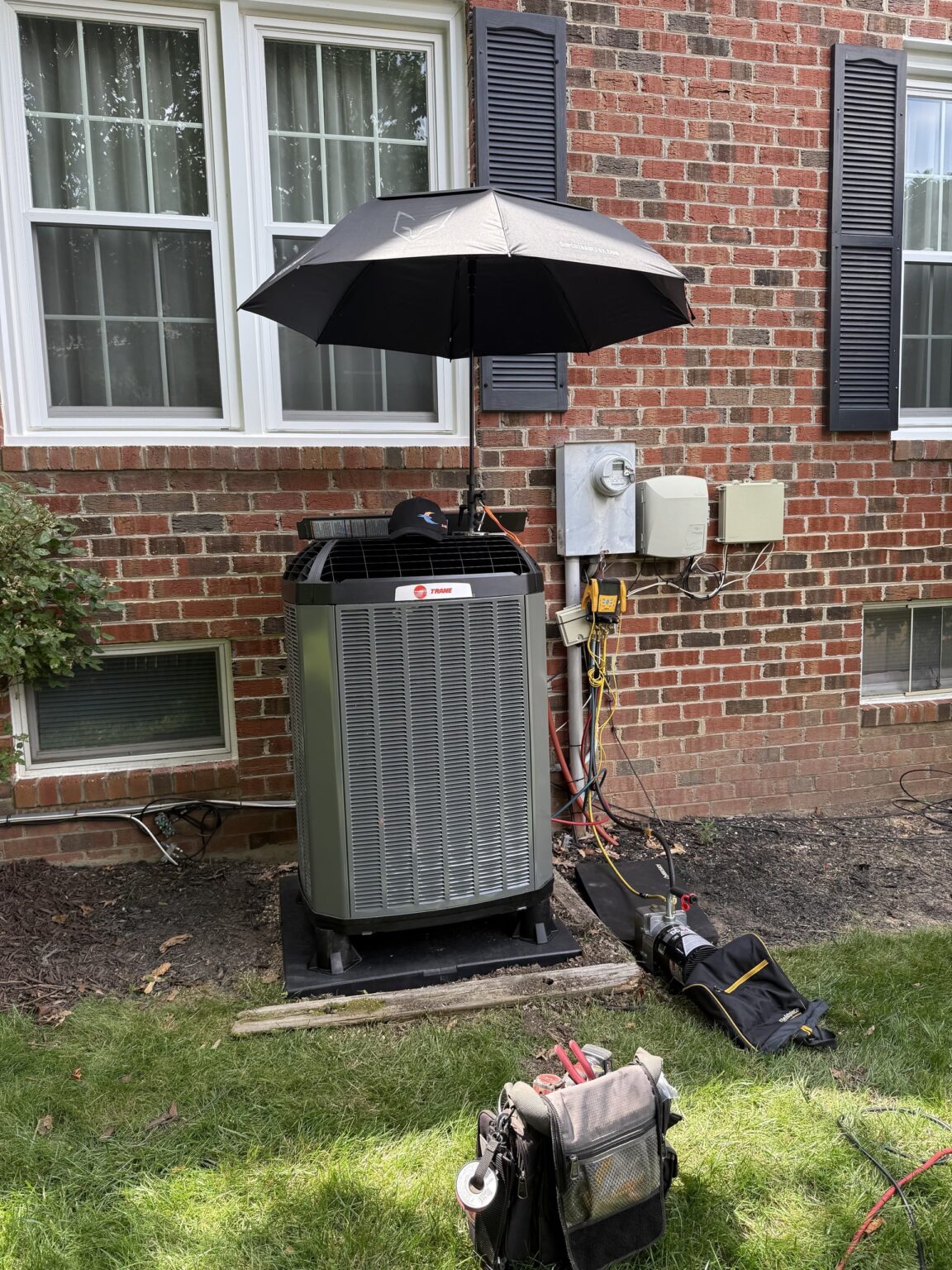 A new Trane outdoor unit beside a brick Northern Virginia home, gauges hooked up and an umbrella shading the work