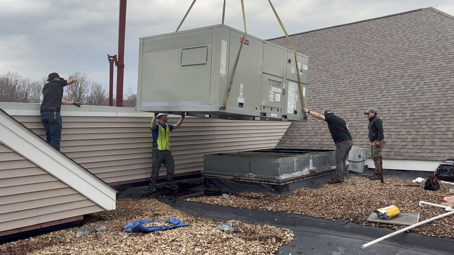 Four workers on a commercial roof in Northern Virginia guiding a Trane packaged rooftop unit down from a crane onto its curb