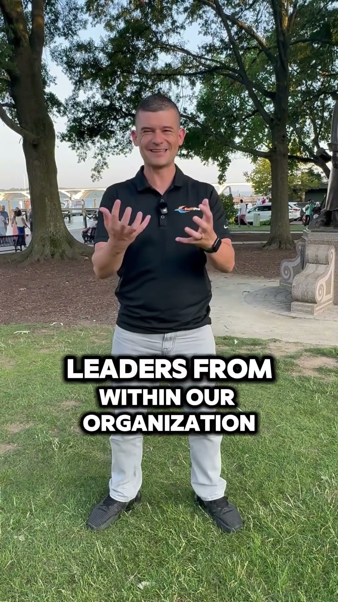 A man in a black SwiftPro polo and light jeans stands on the lawn of a waterfront park at golden hour and talks about growing leaders from within the organization and getting better every day.
