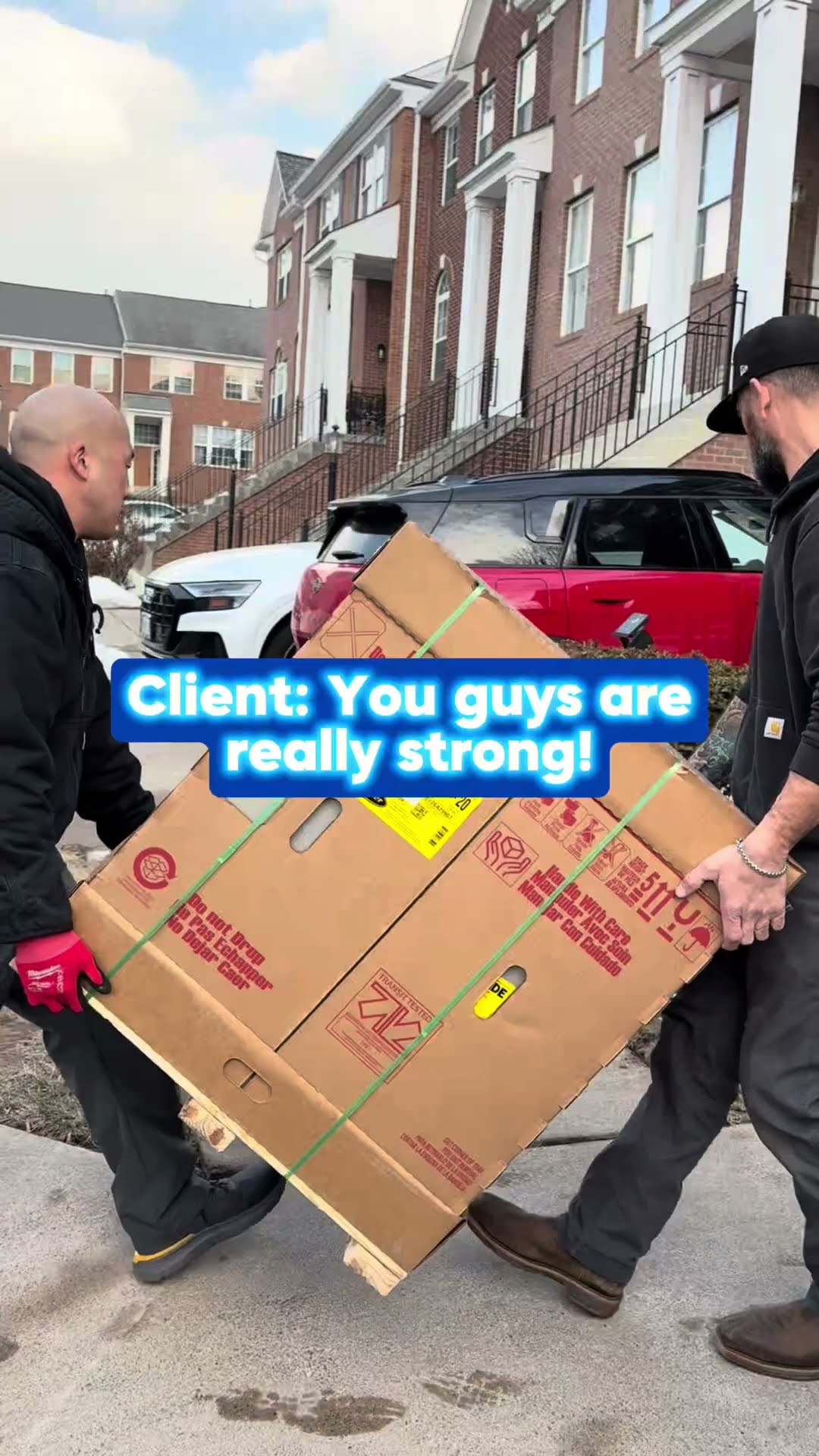 Two techs carry a boxed piece of HVAC equipment along a sidewalk past brick townhouses, and two techs wheel a new AC condenser on a hand truck across a wooden deck.