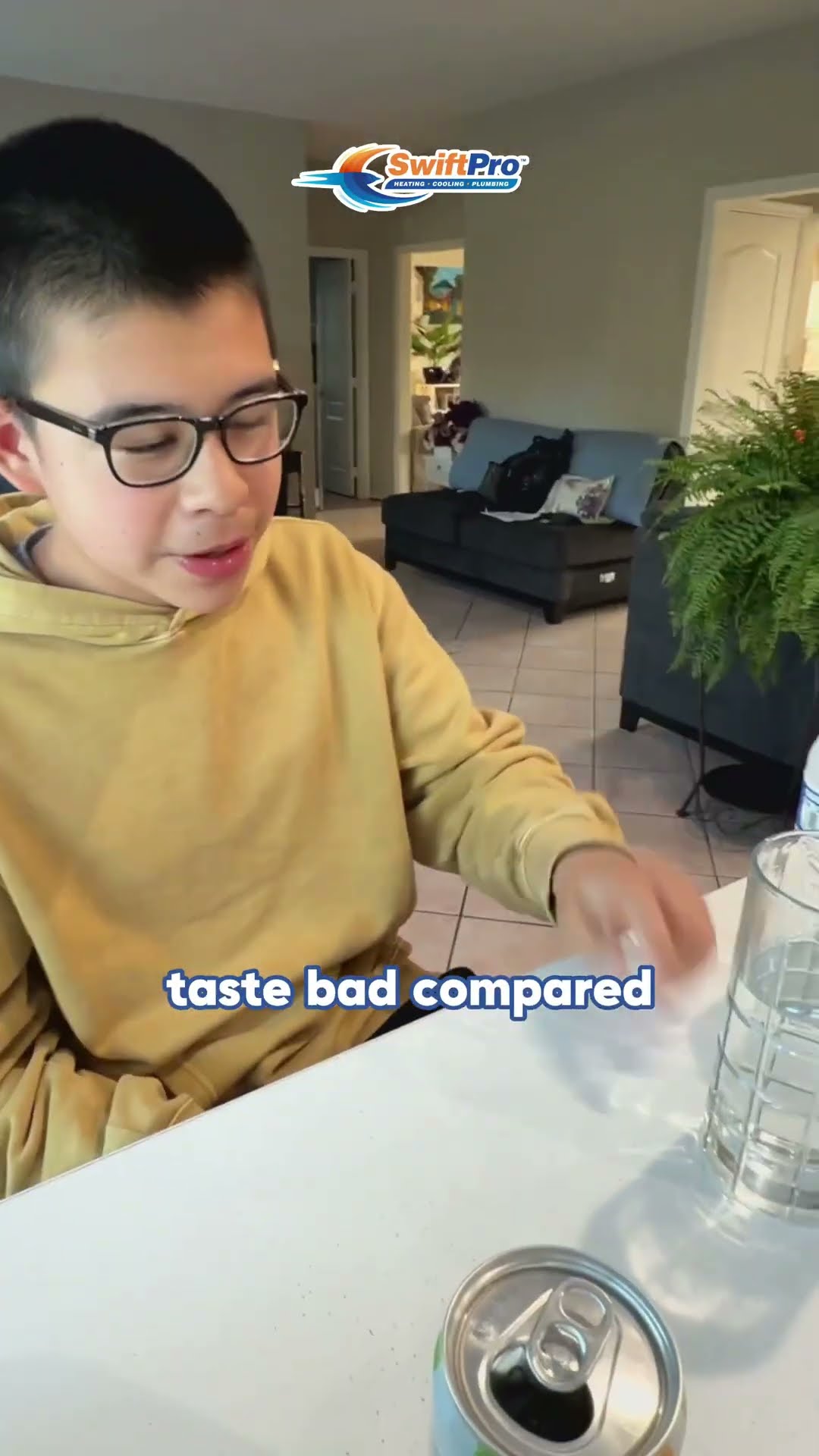 A tap water versus bottled water taste test in a family kitchen: a teen in glasses and a yellow hoodie tastes from glasses at the table while a tech in a black shirt fills glasses at the sink.