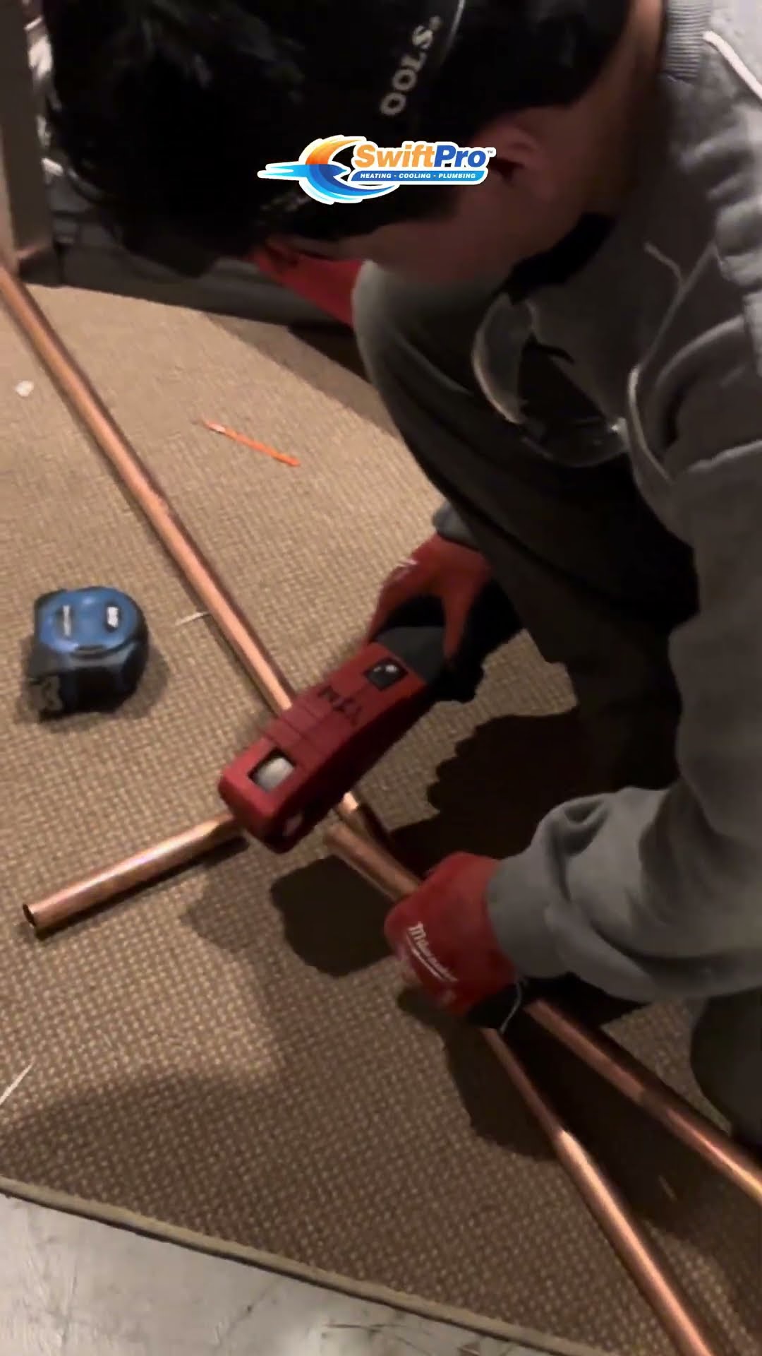 A tech in a gray hoodie cuts copper pipe with a pipe cutter on a drop cloth.