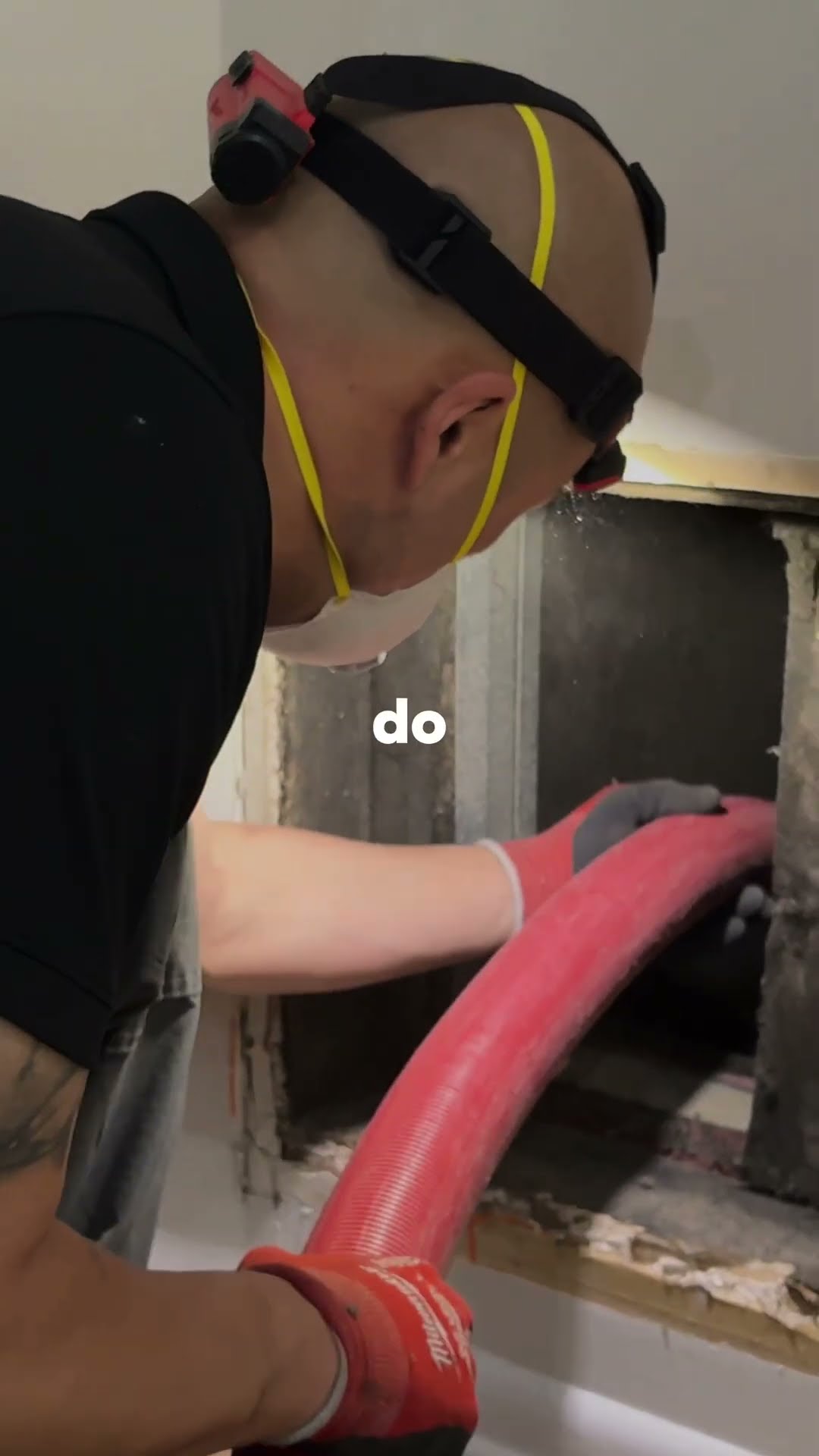 Air duct cleaning: a tech in a headlamp and N95 vacuums a ceiling return with a Milwaukee vac, then feeds a red vacuum hose into a wall return opening on a wood floor.