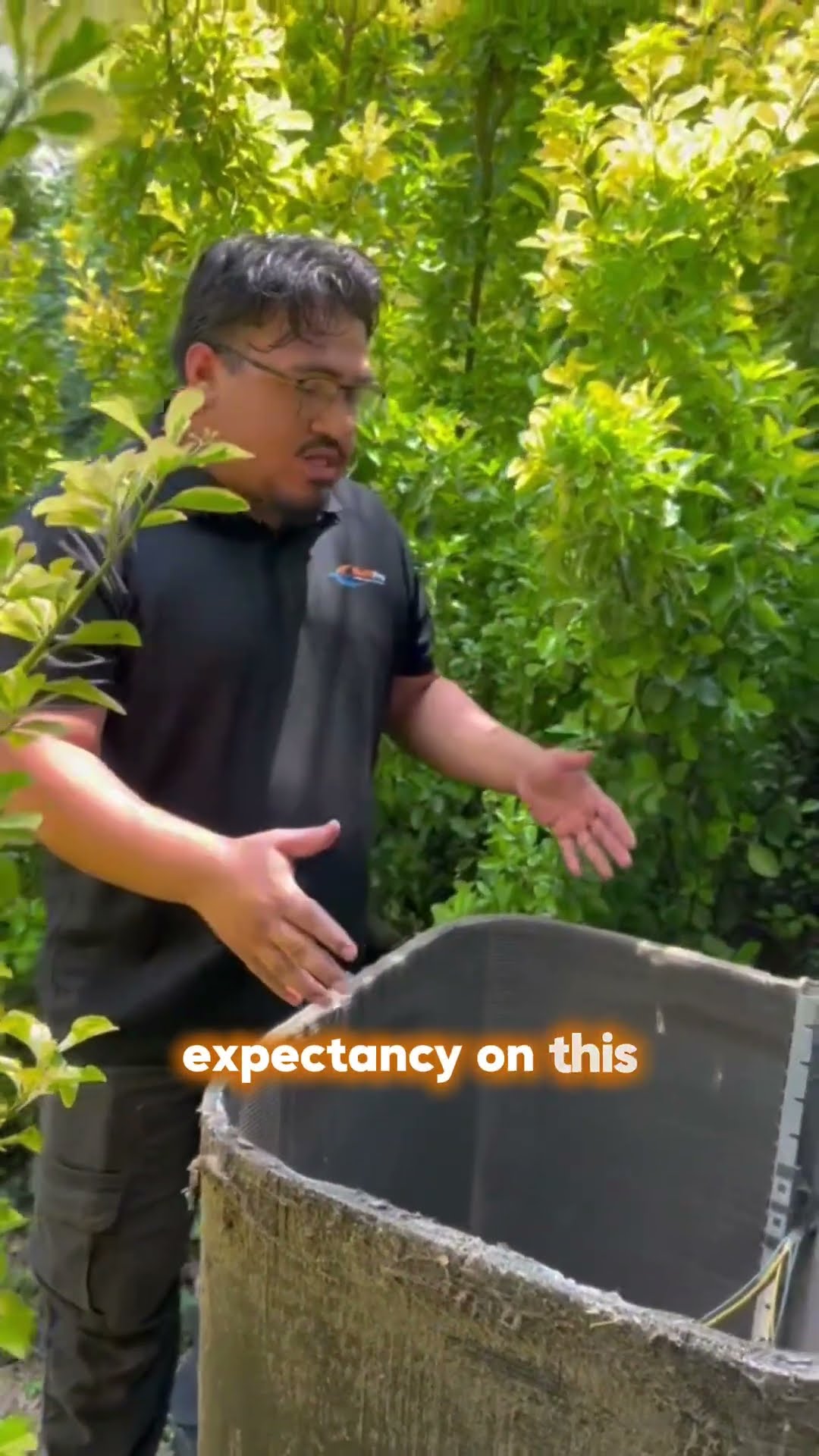 A tech in a black SwiftPro polo and glasses stands in a leafy yard beside an outdoor AC condenser with its top off and explains how a dirty coil shortens the unit's life, pitching a professional coil