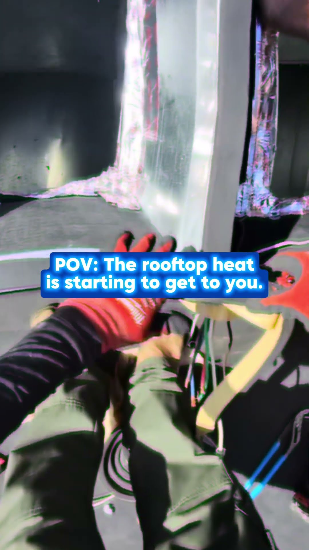 POV of red-gloved hands and olive pants working on sheet metal ductwork at a rooftop unit opening in bright sun.