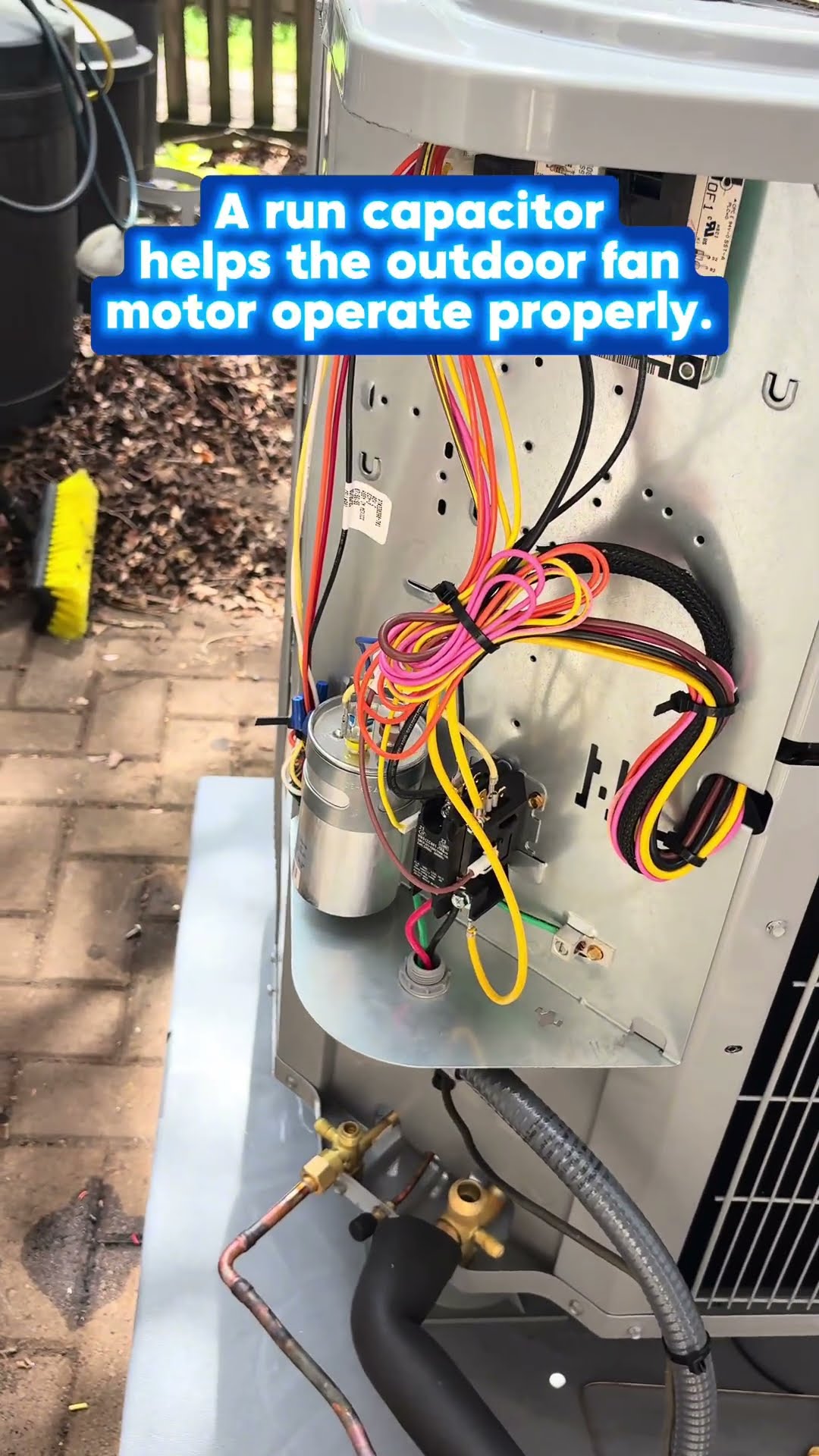 A young tech opens the electrical panel on an outdoor AC condenser beside a house; close-up of the run capacitor and contactor wiring.