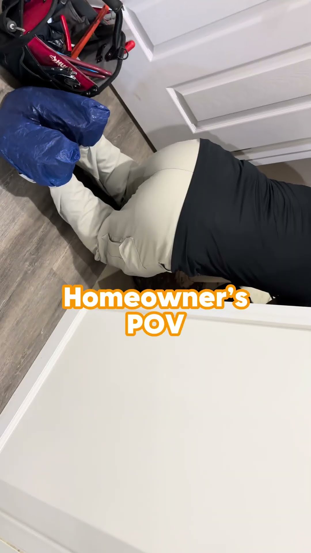 A tech in a black shirt and tan pants kneels at a basement sump pit, fitting white PVC discharge pipe through the black pit lid.
