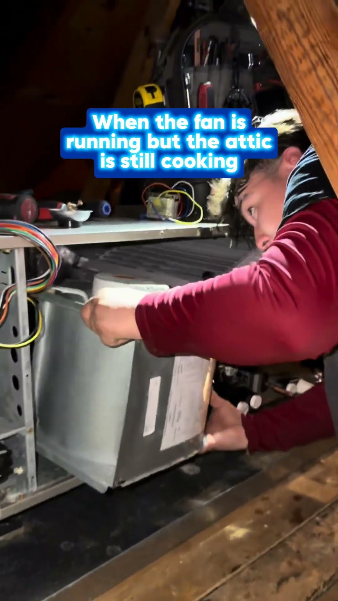 A tech in a red hoodie with a fur-lined hood works on an air handler blower in a hot attic.
