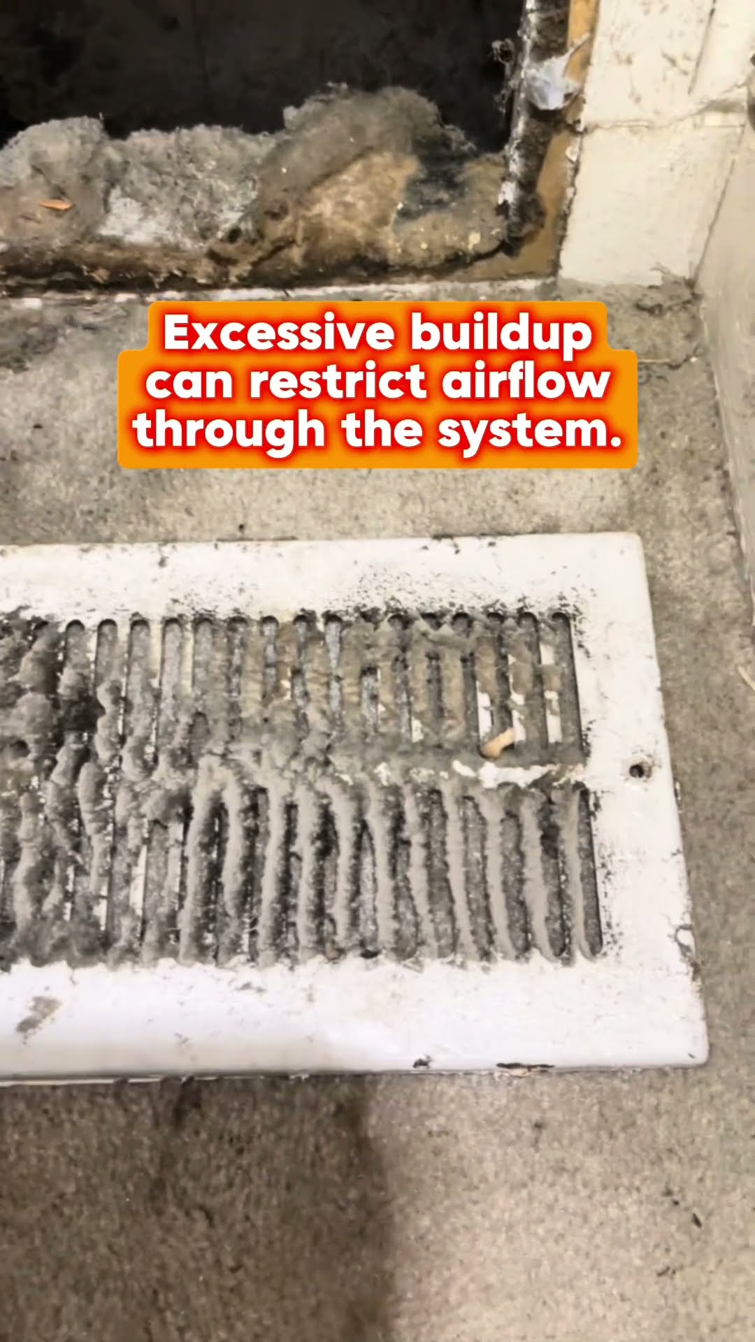 Air duct cleaning: a tech with a headlamp and respirator works at a return in a living room beside a bookshelf, a floor register caked with dust, and a red vacuum hose fed into the duct opening.