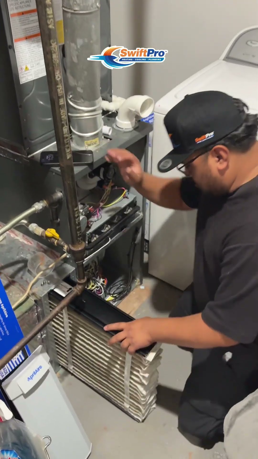 A tech pulls the media filter from an Aprilaire filter cabinet on a gas furnace in a laundry room.