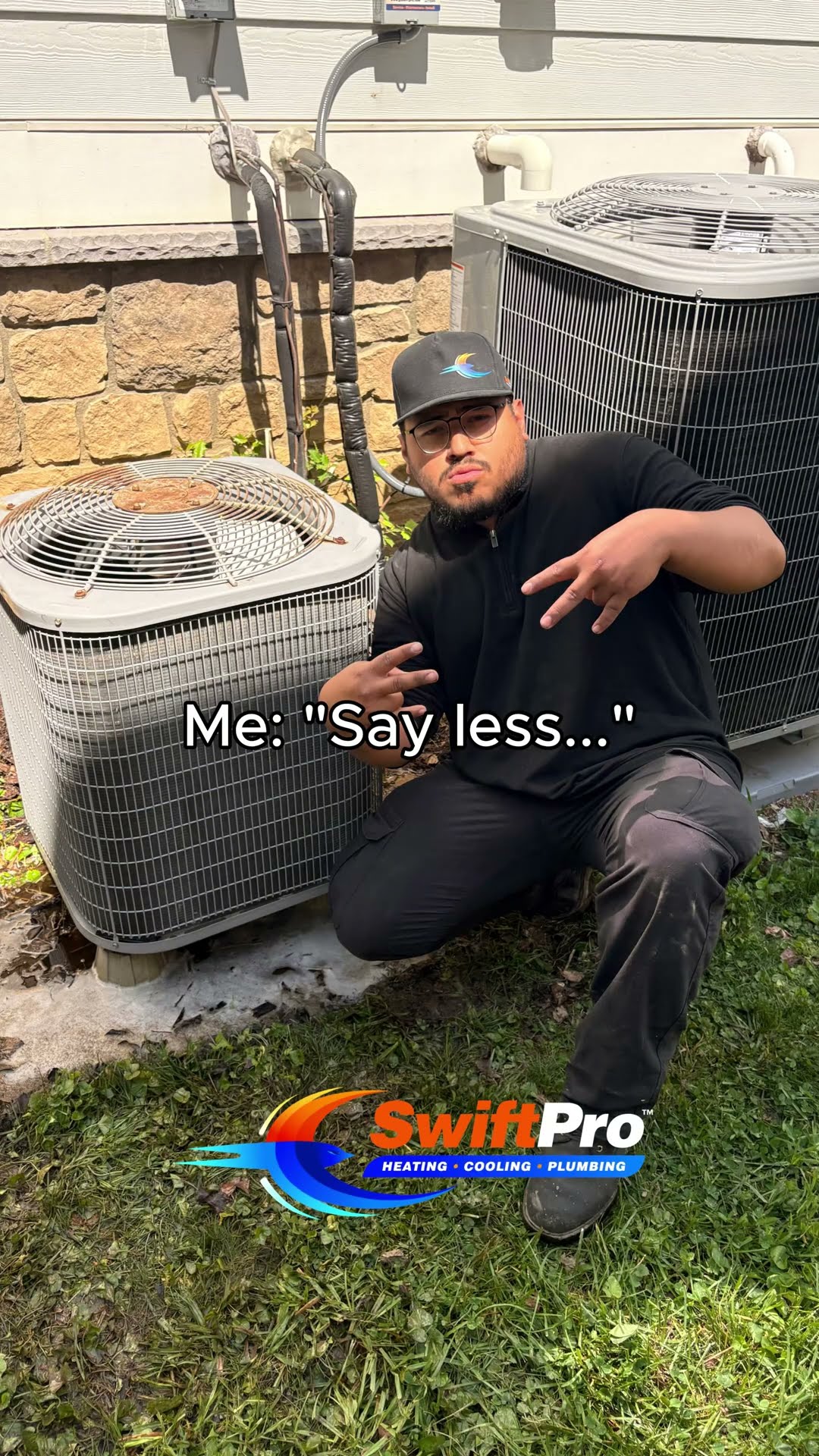A tech in black clothes, black cap and glasses walks across a side yard, then poses and hugs two newly installed outdoor AC condensers on pads against a stone-and-siding house ('Boss: please take pict