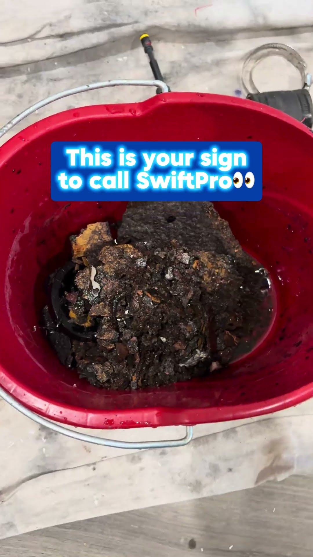 A failed sump pump caked in black sludge sits in a red bucket.