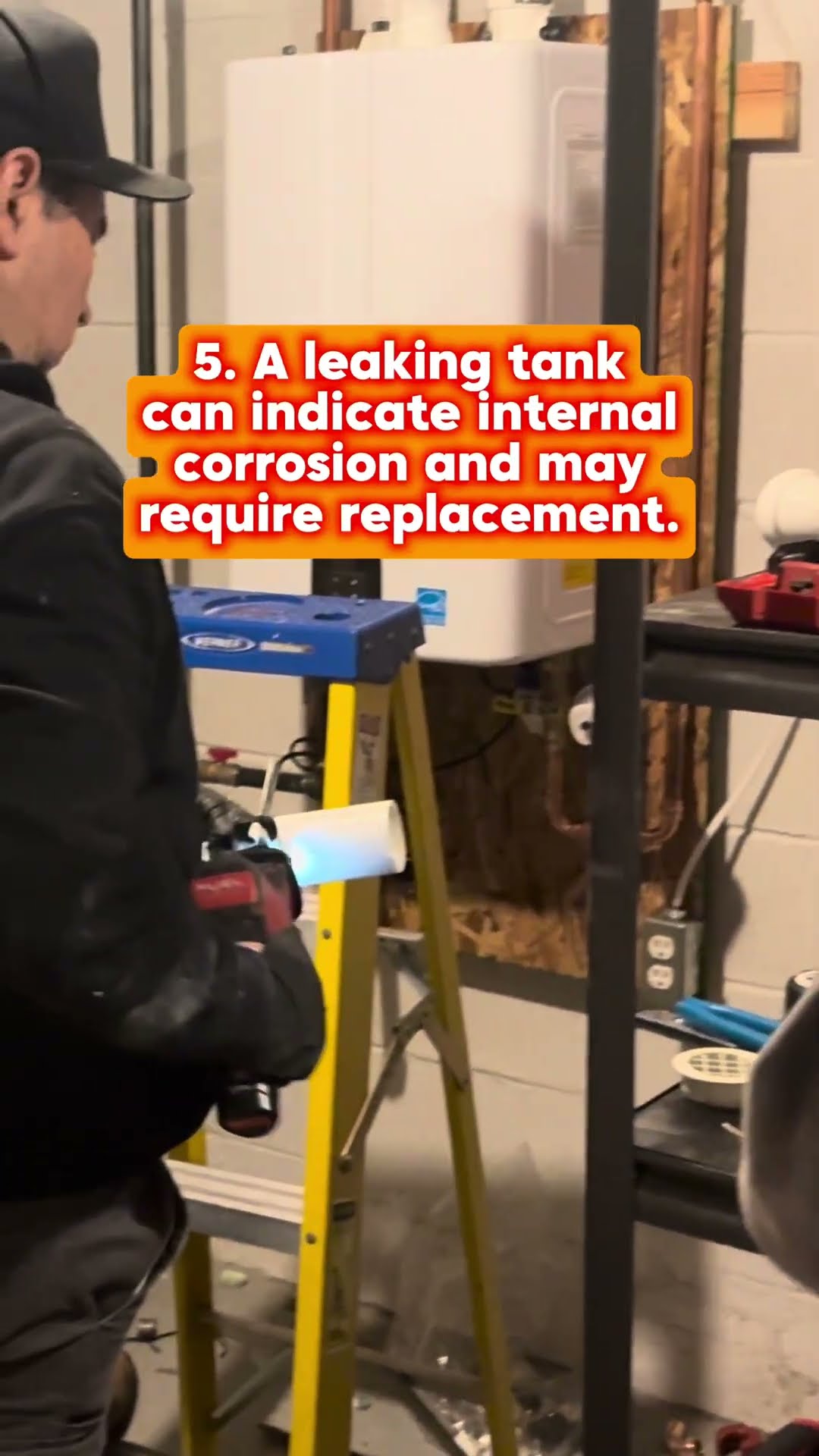 A wall-mounted tankless water heater being installed in a basement: gloved hands connect the piping, a tech on a ladder solders copper with a torch, and new copper and PVC vent piping.