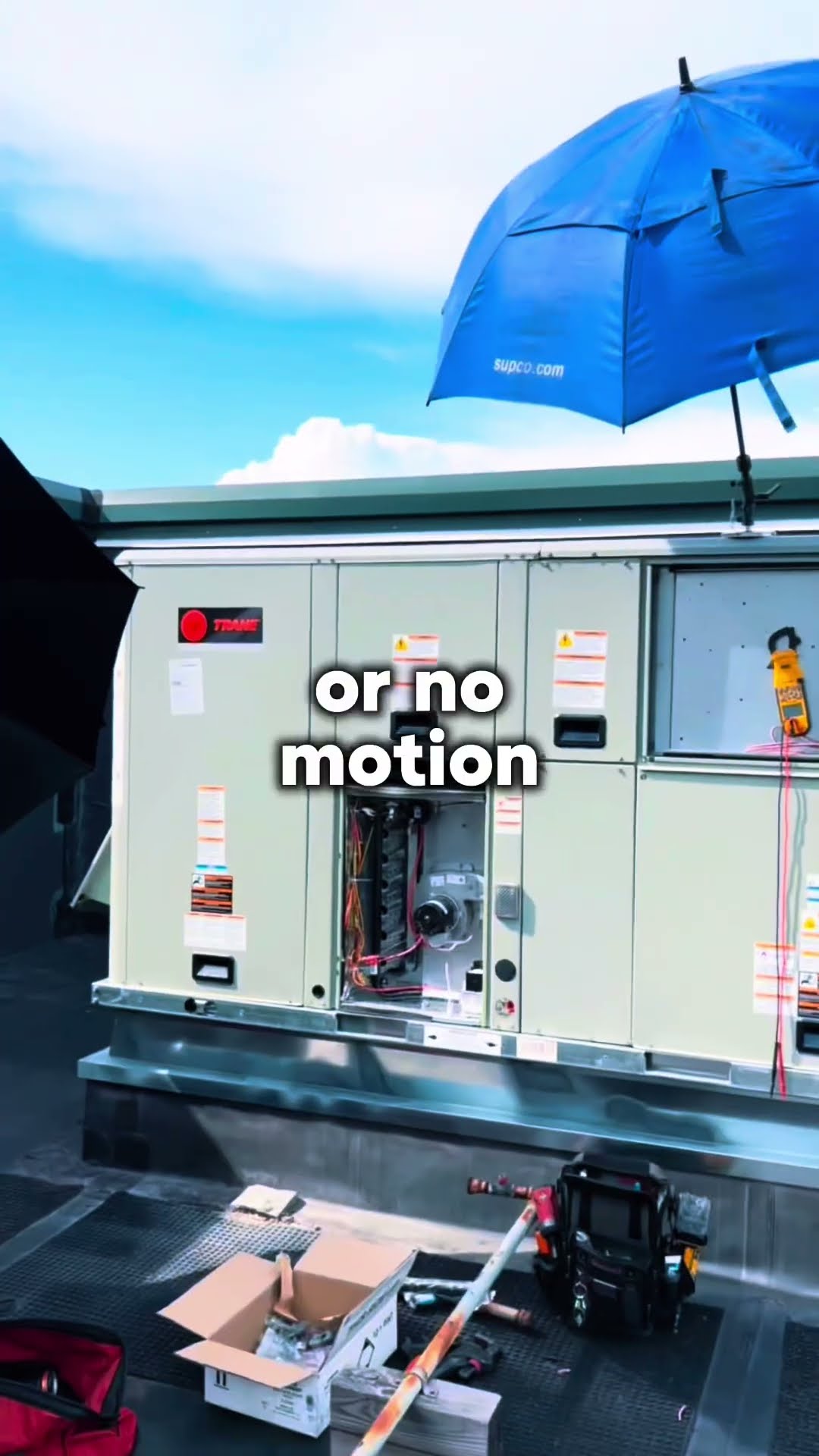 Commercial rooftop: a tech in a royal blue long-sleeve shirt guides a unit section overhead, then a Trane rooftop unit (Trane logo legible) with panels open, a clamp meter clipped on and a blue umbrel