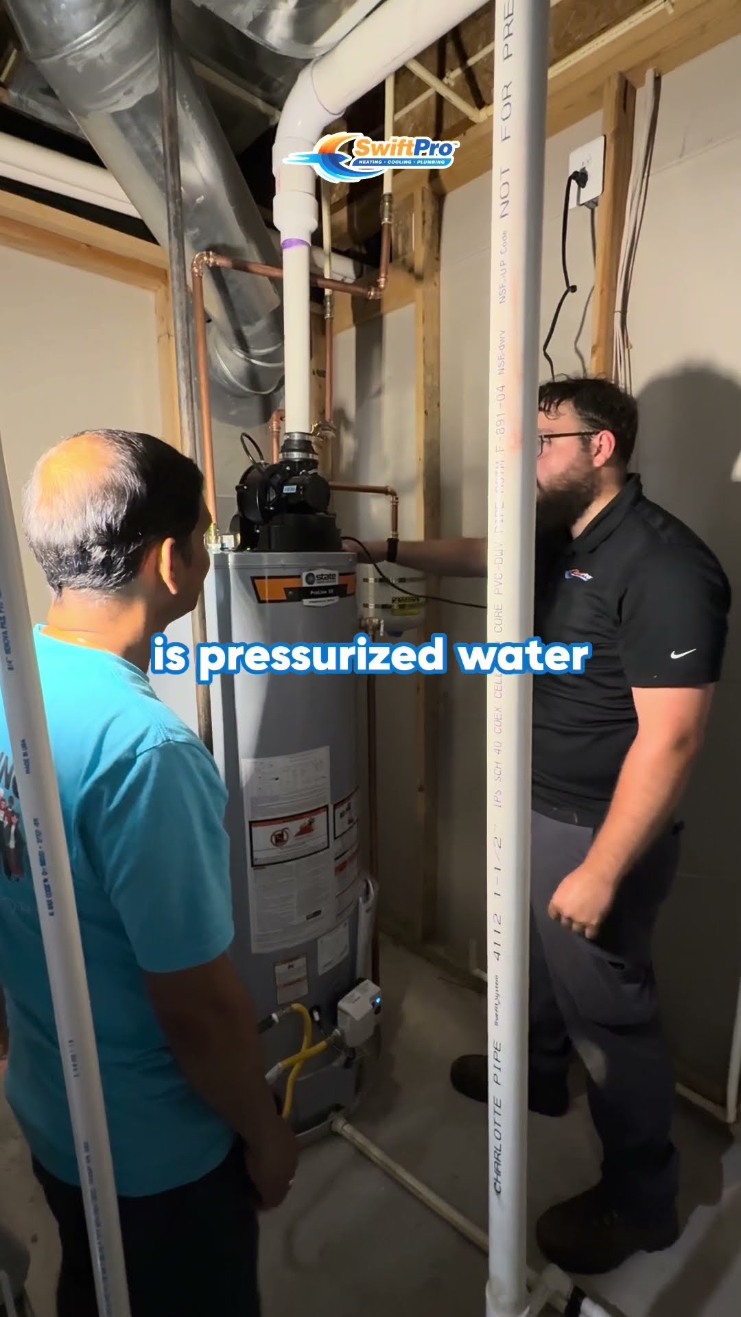 A tech explains a leaking gas water heater to a homeowner in an unfinished basement utility area, pointing to the tank and the gas shutoff.