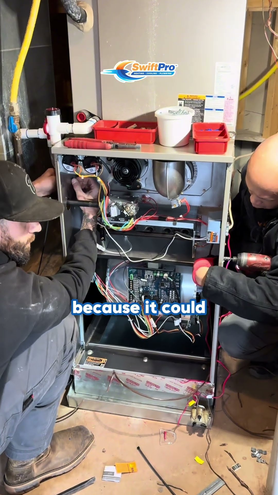 Two techs work inside an opened high-efficiency gas furnace in a basement.